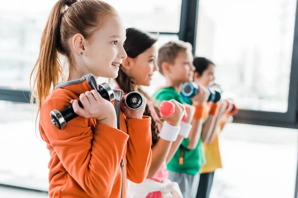 Улыбающиеся дети в спортивной одежде тренируются с гантелями — стоковое фото