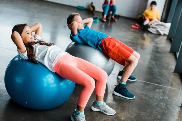 Niños haciendo ejercicios abdominales con pelotas de fitness - foto de stock
