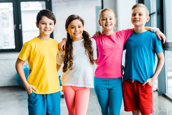 Niños preadolescentes alegres sonriendo y abrazándose en el gimnasio - foto de stock