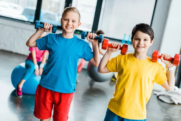 Niños alegres riendo mientras entrenan con pesas — Stock Photo