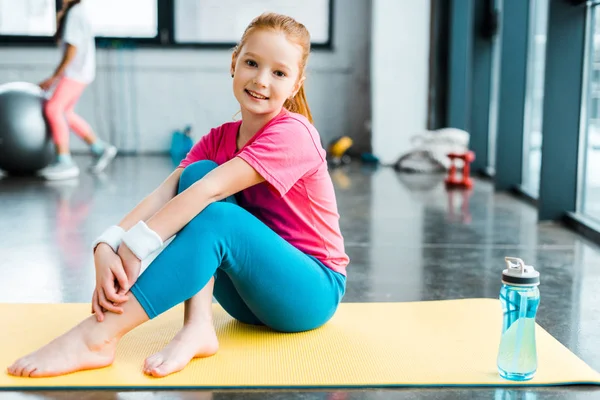 Niño descalzo sentado en una colchoneta de fitness amarilla con sonrisa - foto de stock