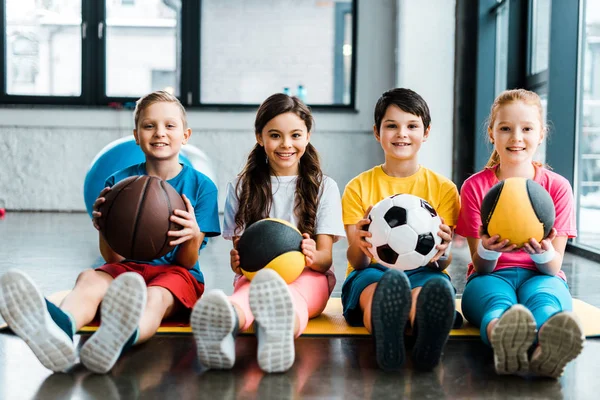 Preteen kids sitting on fitness mat with balls — Stock Photo