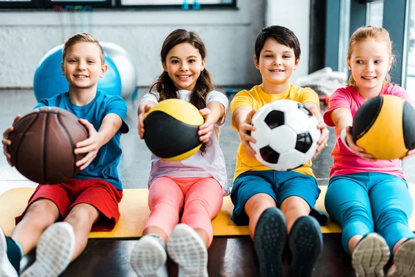 Cheerful kids sitting on fitness mat with balls — Stock Photo
