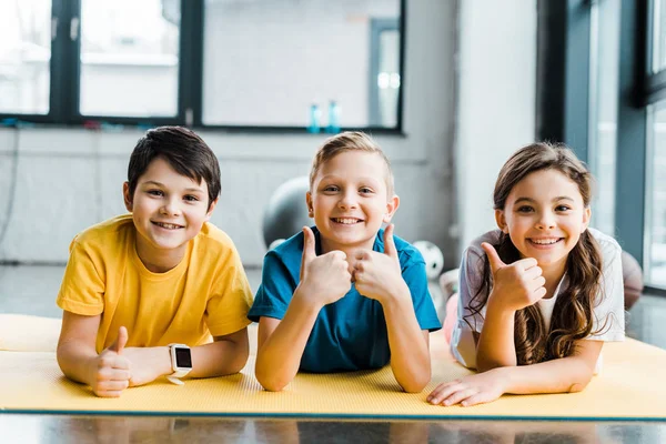 Laughing kids posing on fitness mat with thumbs up — Stock Photo