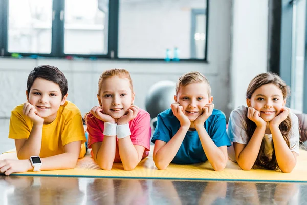 Lindos niños preadolescentes tumbados en la alfombra de fitness y mirando a la cámara - foto de stock