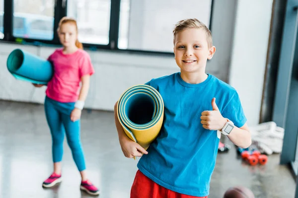 Boy holding fitness mat and showing thumb up — Stock Photo