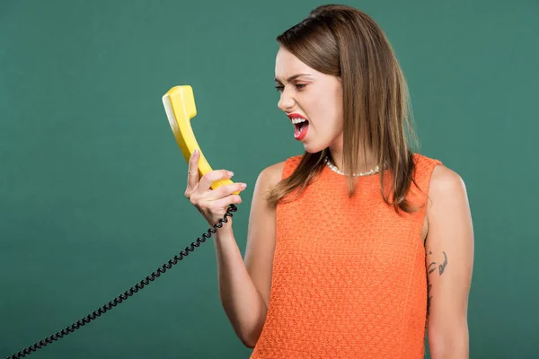 Beautiful angry woman yelling at retro telephone isolated on green — Stock Photo