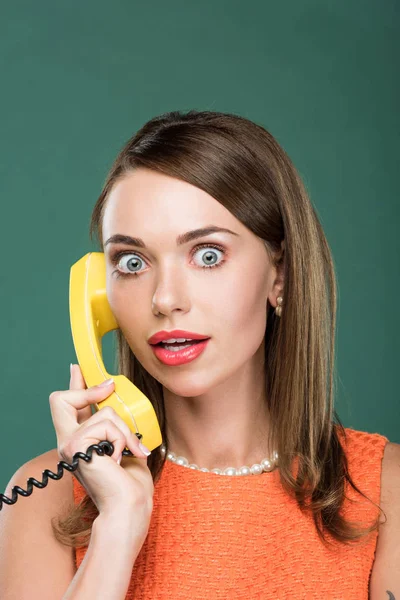 Schöne überraschte Frau, die am Retro-Telefon spricht und isoliert auf grün in die Kamera schaut — Stockfoto