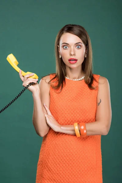 Beautiful shocked woman holding retro telephone and looking at camera isolated on green — Stock Photo