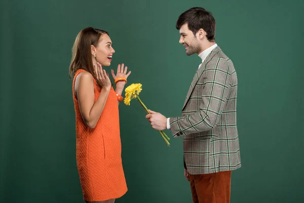 Homem bonito em roupas vintage apresentando flores para bela mulher feliz isolado no verde — Fotografia de Stock