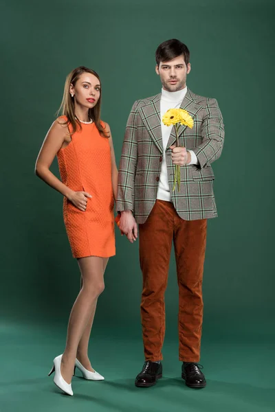 Atractiva pareja en ropa vintage con flores posando sobre fondo verde - foto de stock