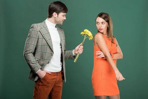 Hombre guapo en ropa vintage presentando flores a mujer insatisfecha aislada en verde - foto de stock