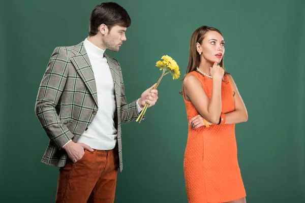 Bel homme en vêtements vintage présentant des fleurs à femme réfléchie isolé sur vert — Photo de stock