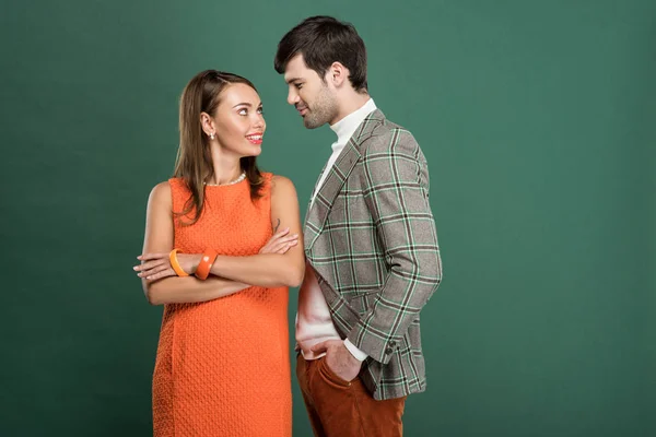 Красивая улыбающаяся пара в винтажной одежде, смотрящая друг на друга изолированно на зеленом — стоковое фото