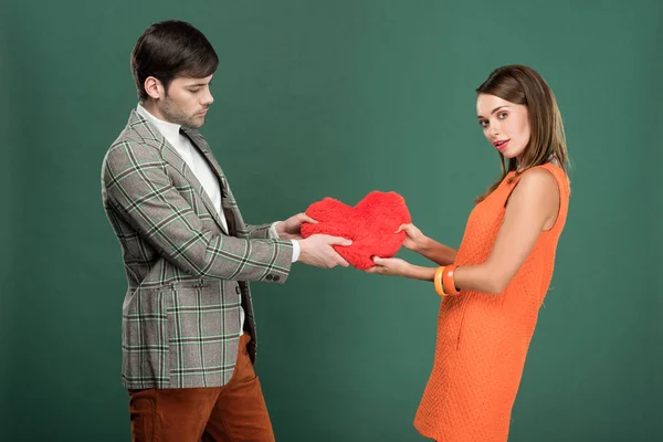Beautiful couple holding heart shaped pillow isolated on green — Stock Photo