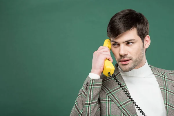 Handsome man in vintage clothes talking on retro telephone isolated on green with copy space — Stock Photo
