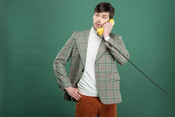 Confused handsome man in vintage clothes talking on retro telephone isolated on green — Stock Photo