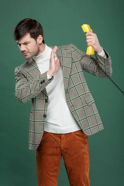 Homem bonito insatisfeito em roupas vintage recusando telefonema e gesticulando com a mão isolada no verde — Fotografia de Stock