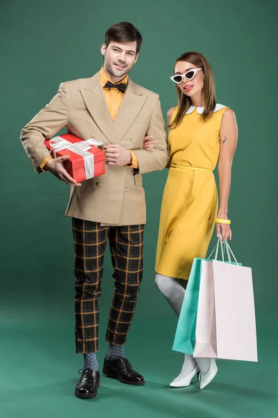 Hermosa pareja en ropa vintage con bolsas de compras y caja de regalo sobre fondo verde - foto de stock