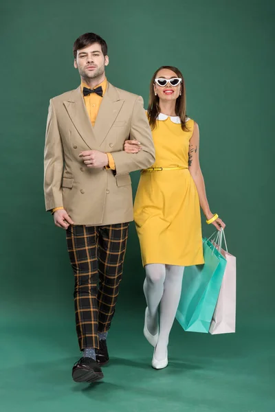 Belo casal em roupas vintage com sacos de compras no fundo verde — Fotografia de Stock
