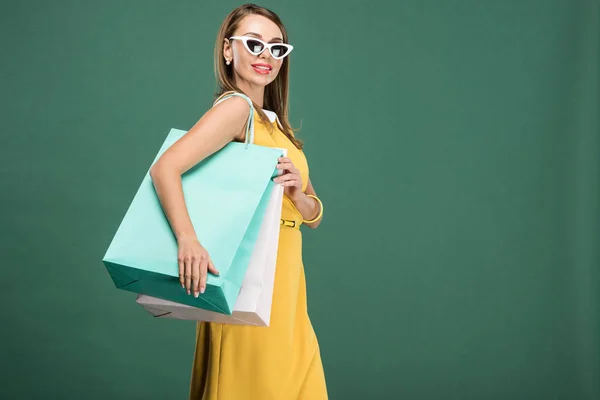 Stylish woman in yellow dress and sunglasses with shopping bags isolated on green — Stock Photo