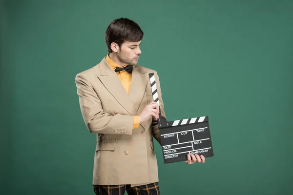 Hombre guapo en ropa vintage sosteniendo película clapperboard aislado en verde - foto de stock