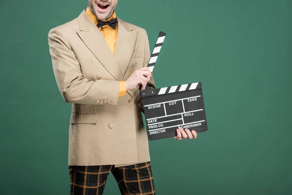 Обрезанный вид взволнованного человека в винтажной одежде, держащего пленку на доске, изолированной на зеленом — стоковое фото