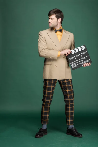 Handsome man in vintage clothes holding film clapperboard on green background — Stock Photo