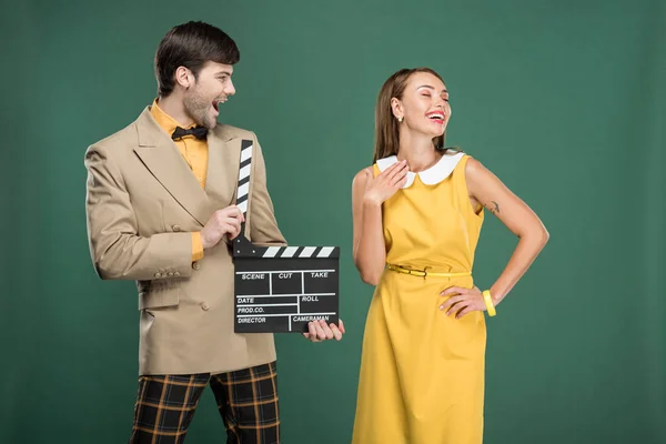 Handsome man in vintage clothes holding film clapperboard while beautiful woman posing isolated on green — Stock Photo