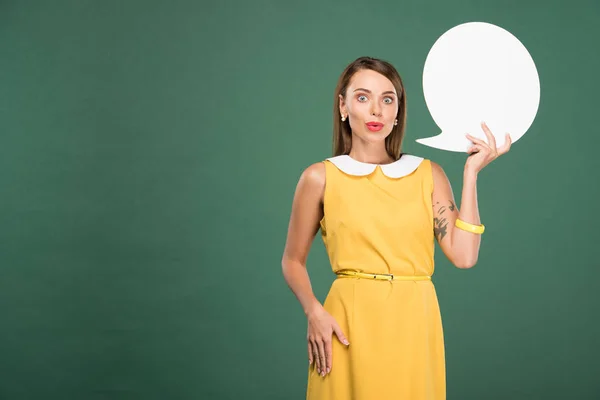 Schöne überraschte Frau in gelbem Kleid hält Sprechblase isoliert auf Grün mit Kopierraum — Stockfoto