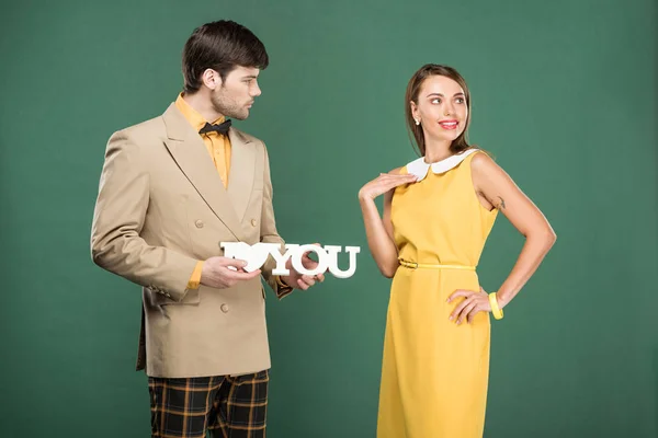 Homem apresentando decorativo 'eu te amo' sinal para mulher bonita em roupas vintage isolado no verde — Fotografia de Stock