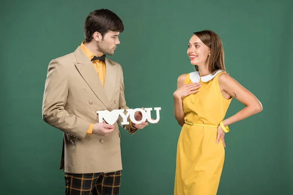 Homem apresentando decorativo 'eu te amo' sinal para bela mulher surpreso em roupas vintage isolado no verde — Fotografia de Stock