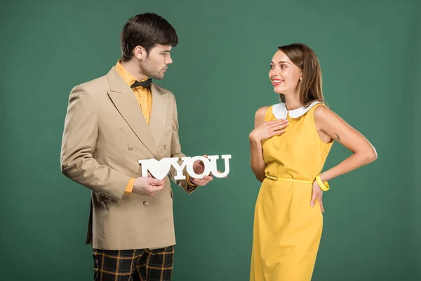 Man presenting decorative 'i love you' sign to beautiful surprised woman in vintage clothes isolated on green — Stock Photo