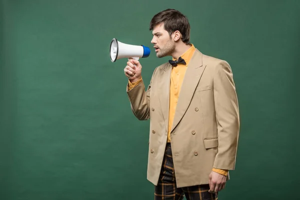 Handsome man in vintage clothes talking in loudspeaker isolated on green with copy space — Stock Photo