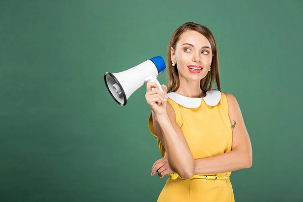 Beautiful stylish woman in yellow dress holding loudspeaker isolated on green with copy space — Stock Photo