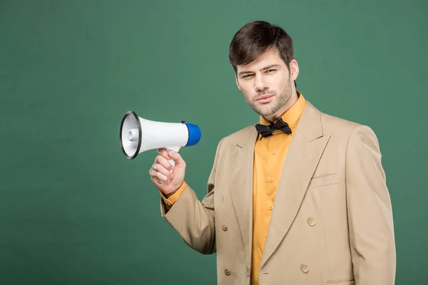 Handsome man in vintage clothes holding loudspeaker and looking at camera isolated on green — Stock Photo