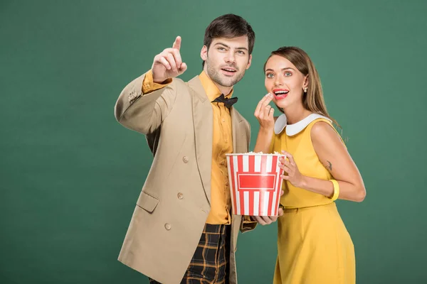 Schönes lächelndes Paar in Vintage-Klamotten, das Popcorn isst, während es sich Film isoliert auf Grün ansieht — Stockfoto