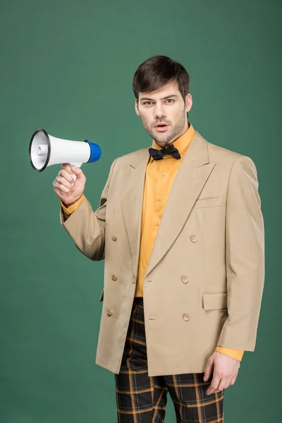 Handsome man in vintage clothes holding loudspeaker and looking at camera isolated on green — Stock Photo
