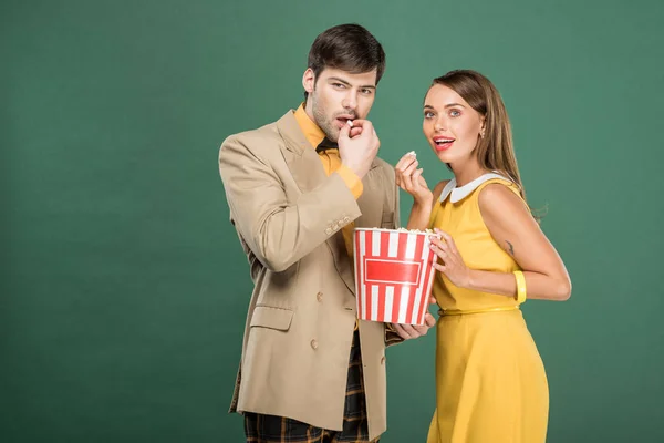 Красивая пара в винтажной одежде ест попкорн во время просмотра фильма изолированы на зеленый — стоковое фото