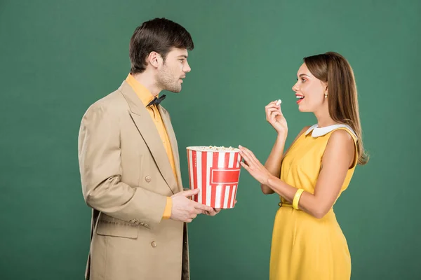 Beau couple en vêtements vintage manger pop-corn et regarder les uns les autres isolé sur vert — Photo de stock