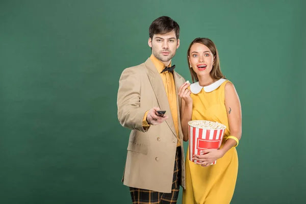 Beautiful couple in vintage clothes with remote control and popcorn watching movie isolated on green — Stock Photo