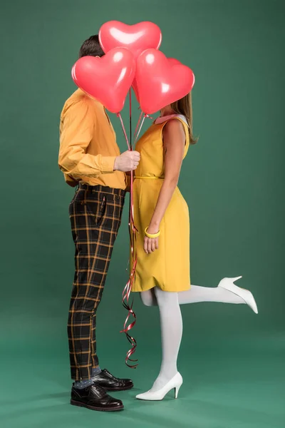 Pareja cubriendo caras con globos en forma de corazón sobre fondo verde - foto de stock