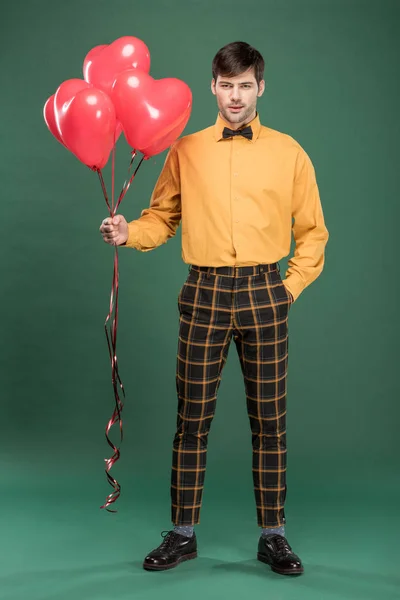 Handsome man in vintage clothes with heart shaped balloons on green background — Stock Photo