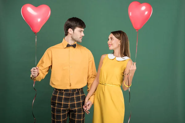 Schönes Paar hält Hände und herzförmige Luftballons isoliert auf grün — Stockfoto