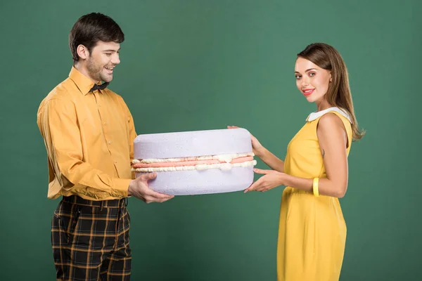 Beautiful smiling couple in vintage clothes holding macaroon model isolated on green — Stock Photo