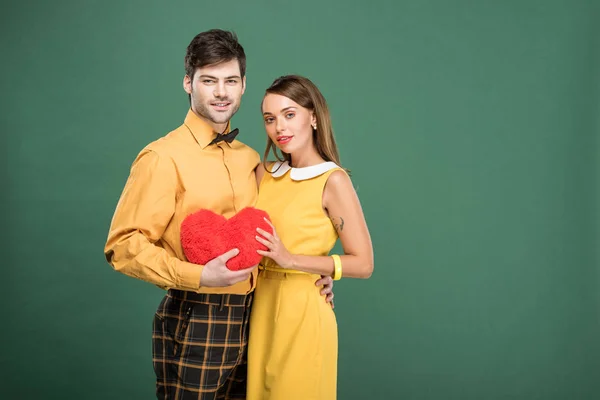 Belo casal segurando travesseiro em forma de coração e olhando para a câmera isolada no verde com espaço de cópia — Fotografia de Stock