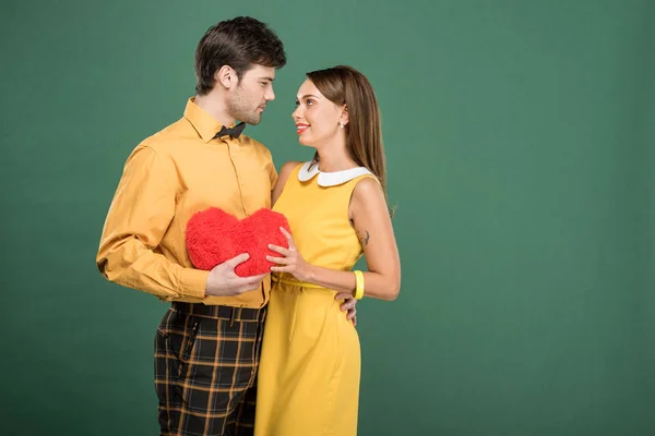 Beautiful couple holding heart shaped pillow isolated on green with copy space — Stock Photo