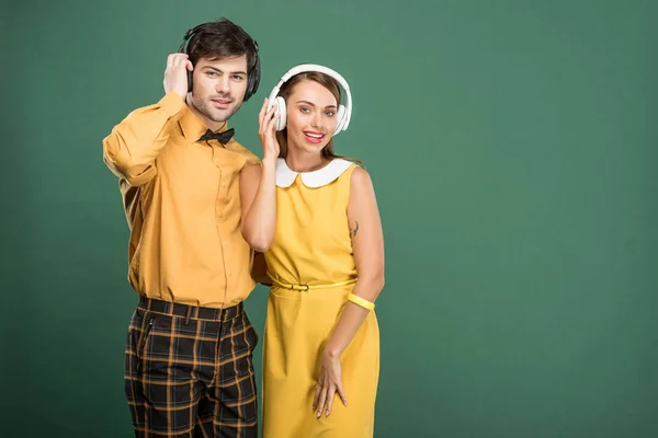 Beautiful happy couple in vintage clothes with headphones isolated on green — Stock Photo