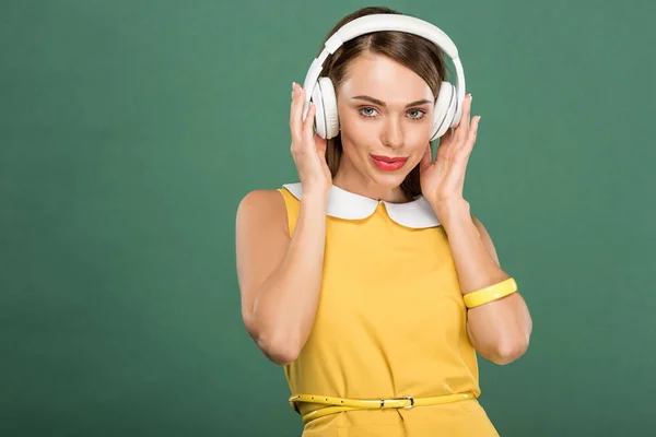 Beautiful stylish woman in yellow dress and headphones looking at camera isolated on green — Stock Photo