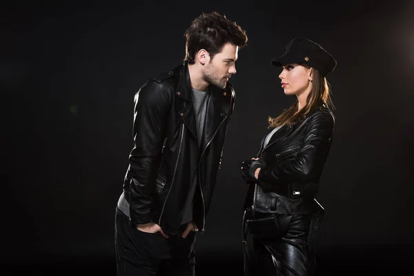 Beautiful couple in leather jackets looking at each other and posing on black background — Stock Photo